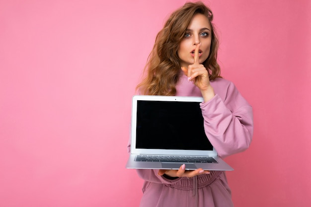 Ritratto del primo piano di bella giovane donna riccia bionda scura che tiene il computer portatile che esamina macchina fotografica