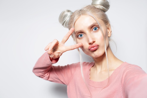 Closeup portrait of beautiful girl making selfie showing peace sign on white