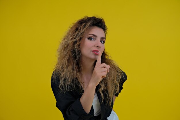 Closeup portrait beautiful girl on a yellow background woman showing finger silence girl showing shh sign keep secret