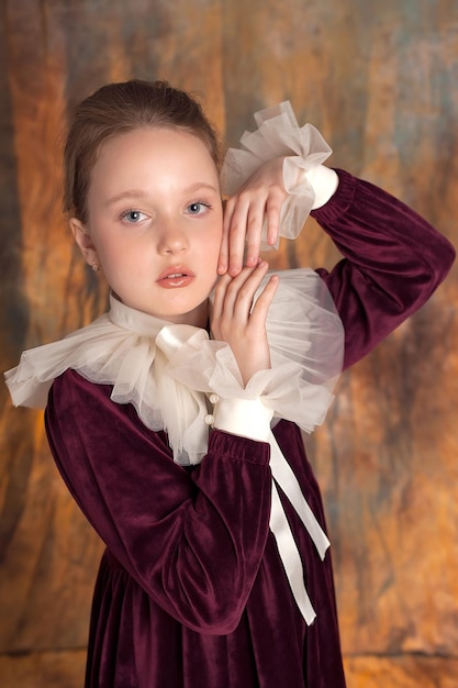 Closeup portrait of a beautiful little girl in a burgundy vintage dress and collar with cuffs The artwork of a romantic womanA cute model of tenderness looks into the camera