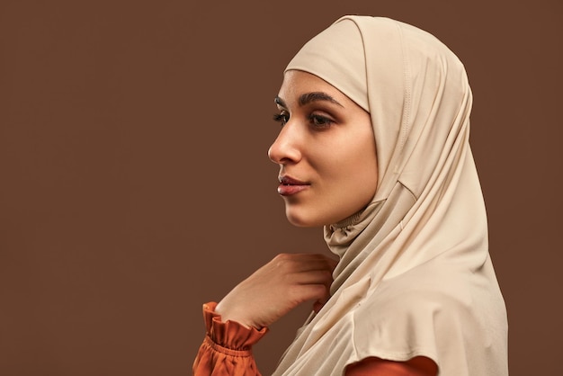 Closeup portrait beautiful muslim woman in beige hijab brown background woman looks awayCopy space