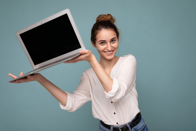 Портрет крупным планом красивой улыбающейся счастливой молодой женщины, держащей компьютерный ноутбук, смотрящую в камеру