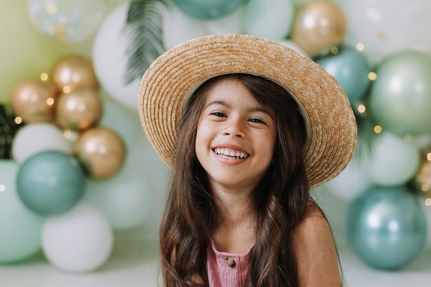 Closeup portrait of a beautiful smiling little girl with brown eyes and dark hair in a straw hat