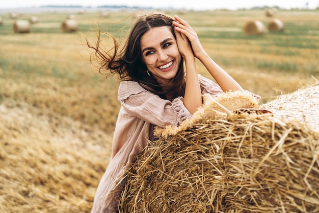Closeup portrait of beautiful smiling woman with closed eyes. The brunette leaned on a bale of hay. A wheat field on the background