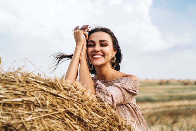 Closeup portrait of beautiful smiling woman with closed eyes. The brunette leaned on a bale of hay. A wheat field