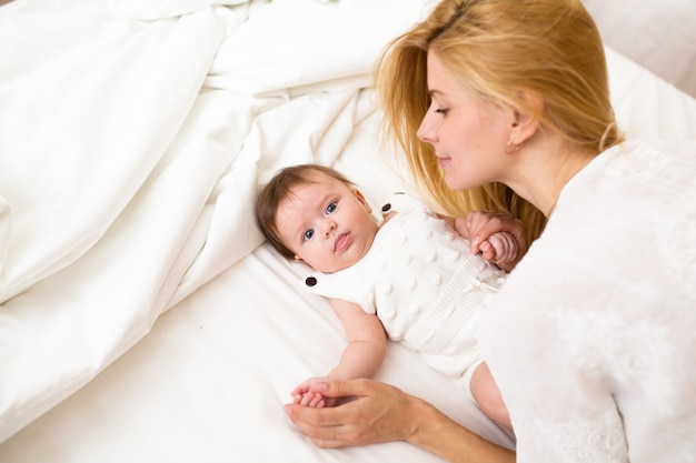 Photo closeup portrait of beautiful young mother with long blond hair cuddling with her adorable 3 months old baby girl