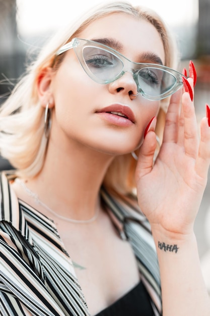 Closeup portrait of a beautiful young stylish girl in fashionable blue glasses and a summer shirt with a top in the city