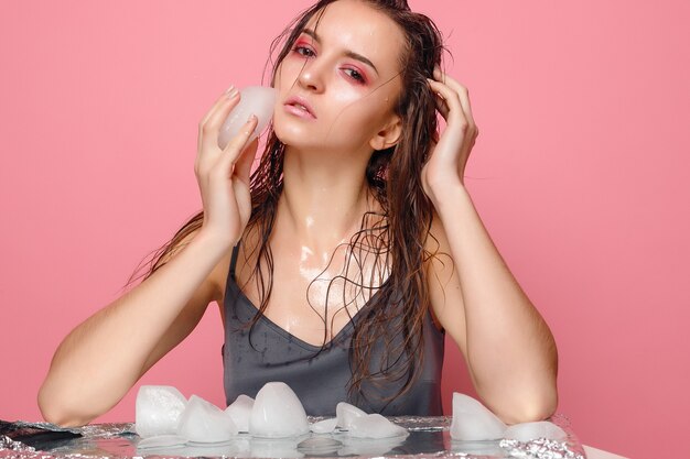 美しい若い女性のポートレート、クローズ アップがピンクの顔に氷を適用します。
