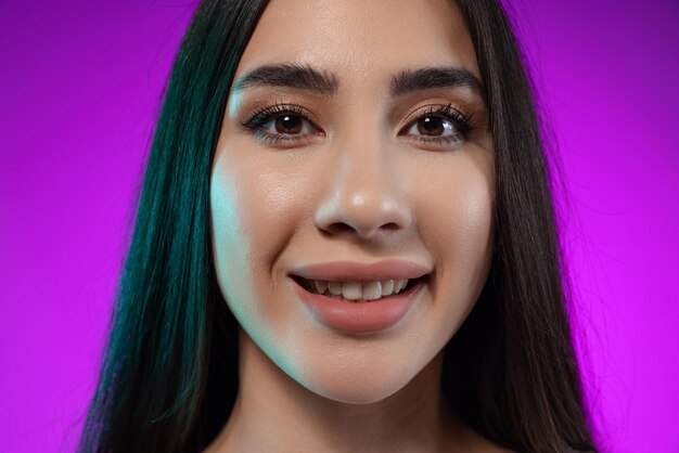 Closeup portrait of beautiful young woman tenderly smiling at camera isolated over purple background