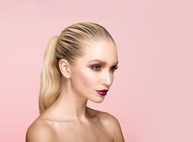 Closeup portrait of beautiful young woman with perfect makeup and hair straightened posing in studio isolated light pink background