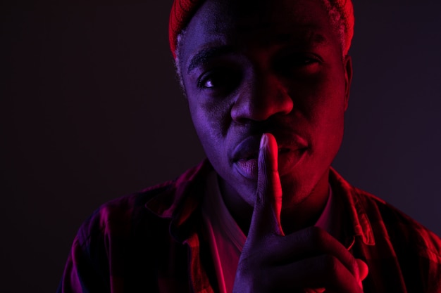 Closeup portrait of a black dreaming African man with big lips showing be quieter in neon light