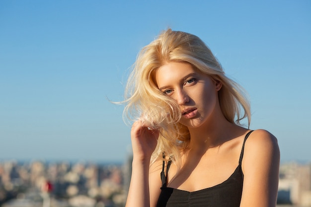 Closeup portrait of blonde woman with natural makeup posing at the roof in sunny evening. Copyspace