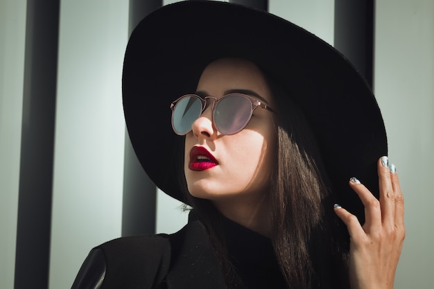 Closeup portrait of brunette woman with bright makeup and shiny hair wears hat and sunglasses