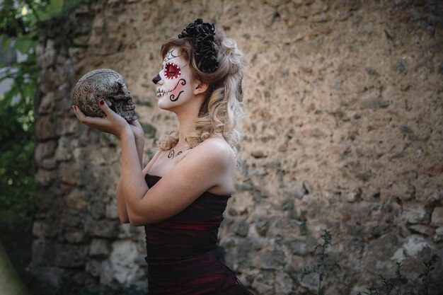 Closeup portrait of calavera catrina young woman with sugar skull makeup dia de los muertos day of the dead halloween in the forest with skull