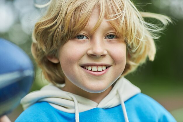 Closeup portrait of carefree blonde boy looking at camera outoors and smiling happily