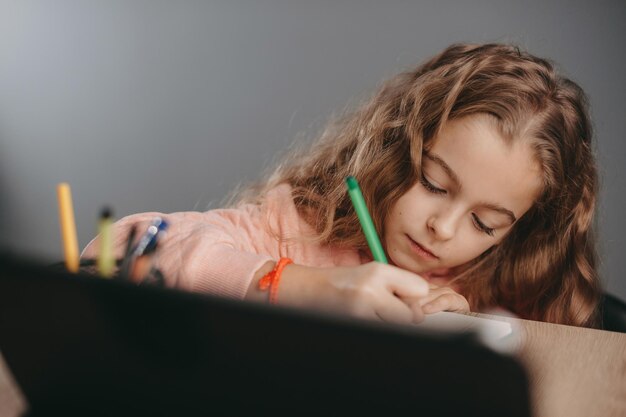 Closeup portrait of a caucasian schoolgirl doing her homework using gadgets for learning girl studyi...