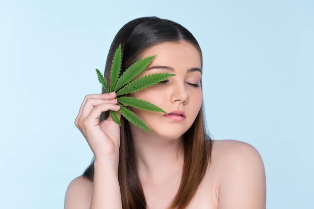 Closeup portrait of charming plump girl with fresh skin holding cannabis leaf