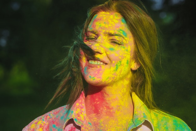 Ritratto del primo piano di un allegro modello bruna coperto da vernice holi rosa e gialla