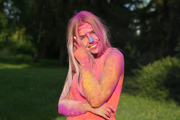 Closeup portrait of cheerful woman posing covered with a colorful dry paint at the park