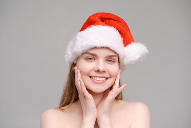 Closeup portrait cheerful young woman in red Santa Claus outfit touches her