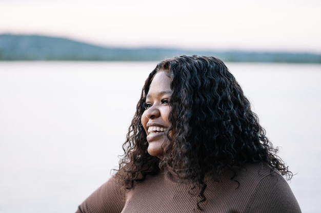 Closeup portrait curly african afro american dark skin woman look away near lake outside Interracial female Copy space