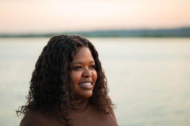 Closeup portrait curly african afro american dark skin woman look away near lake outside Interracial female Copy space