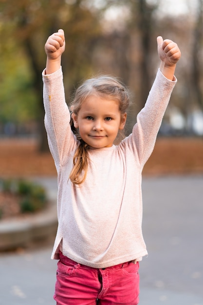 Closeup portrait of cute adorable smiling little Caucasian girl child standing in autumn fall park outside