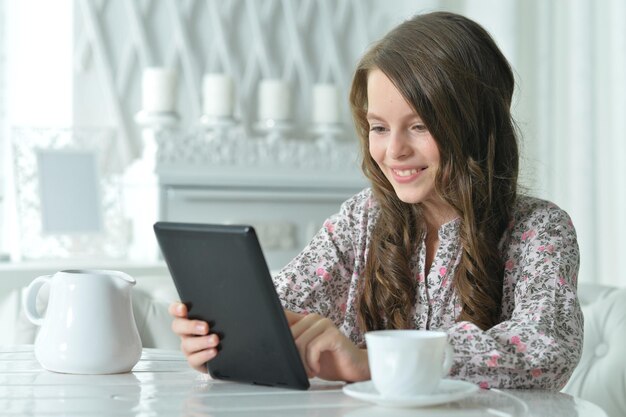 Closeup portrait of cute girl using tablet while drinking tea at light kitchen