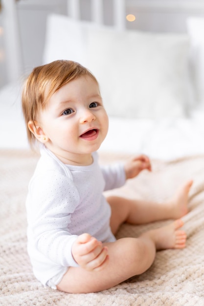 Photo closeup portrait of a cute little baby girl in a bright room in white clothes at home on a bed the concept of childrens goods