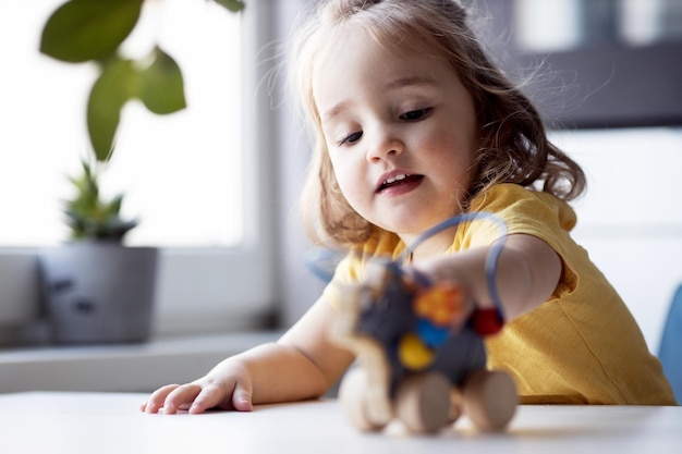 Photo closeup portrait of cute little girl playing with toy kid in yellow tshort excited game