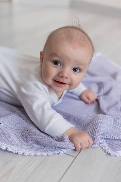 Closeup portrait of a cute newborn baby lying on his stomach on a lilac blanket on the floor