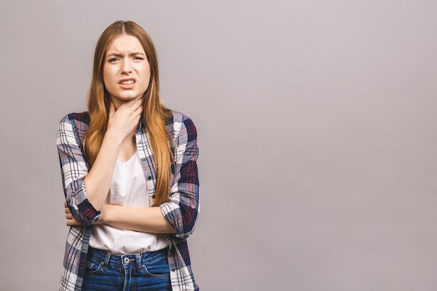 Closeup portrait of cute sick young blonde woman in casual having sore throat, holding hand on her neck/Throat pain, painful swallowing concept/ Inflammation of the upper respiratory tract.