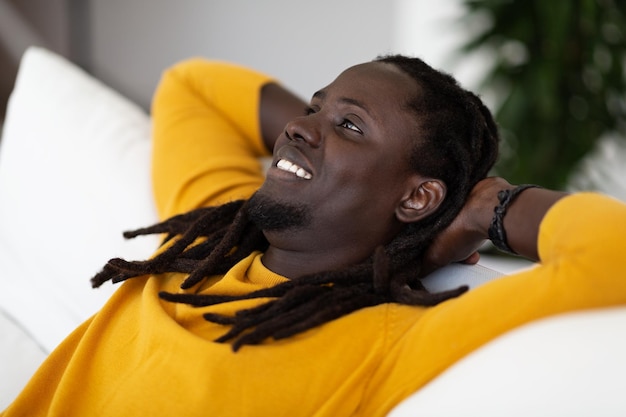 Closeup Portrait Of Dreamy Black Man Leaning Back On Couch And Smiling