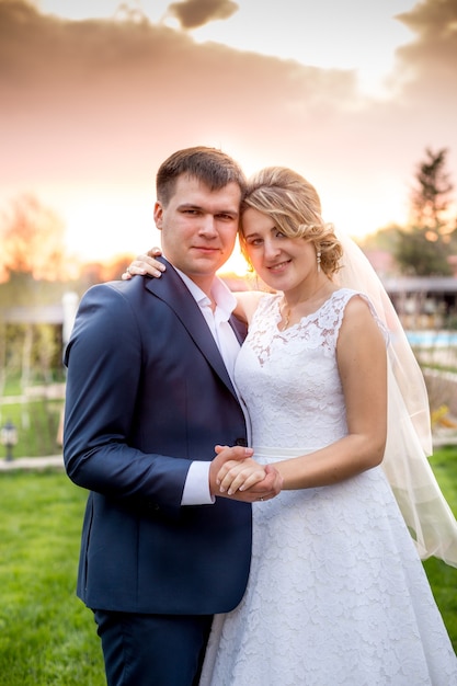 Closeup portrait of elegant newlyweds hugging at park at sunset