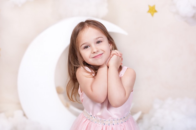 Ritratto del primo piano del fronte della bambina con capelli lunghi. bella bambina su un muro di luna, stelle e nuvole. il bambino sta sognando. il bambino è felice. ragazza carina sorridente. concetto di infanzia