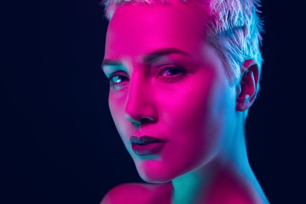 Closeup portrait of female fashion model in neon light on dark studio background