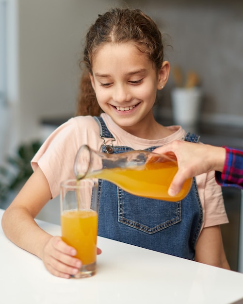 Il ritratto del primo piano di una mano femminile versa il succo d'arancia sveglio della bambina.