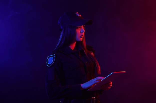 Closeup portrait of a female police officer posing for the camera against a black background with re...