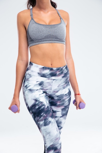 Closeup portrait of a fitness woman`s body with dumbbells isolated on a white wall