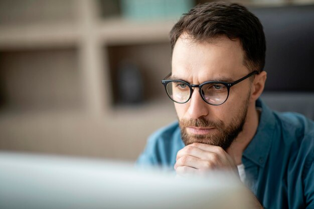 Closeup portrait of focused handsome young man in eyeglasses working on laptop