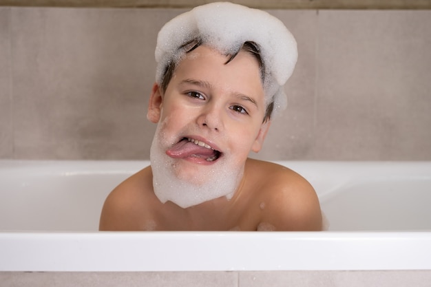 Closeup portrait of funny boy playing with water and foam in bathroom Cute happy child bathe and makes funny faces healthy childhood