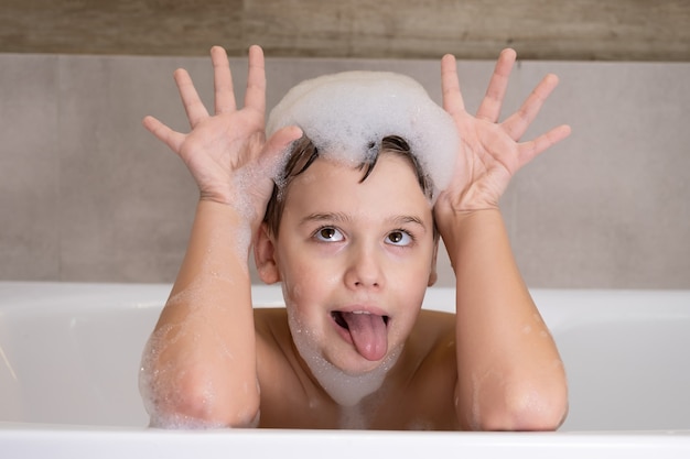 Photo closeup portrait of funny boy playing with water and foam in bathroom cute happy child bathe