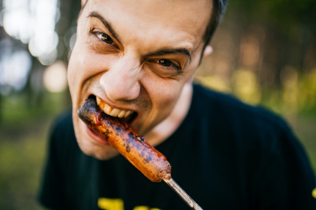 Closeup portrait of  funny man eating sausage with expression.