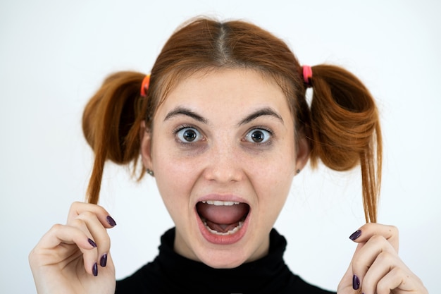 Closeup portrait of a funny redhead teenage girl with childish hairstyle smiling happily isolated