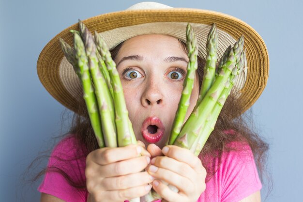 Photo closeup portrait of funny surprised woman is holding asparagus in front of her face