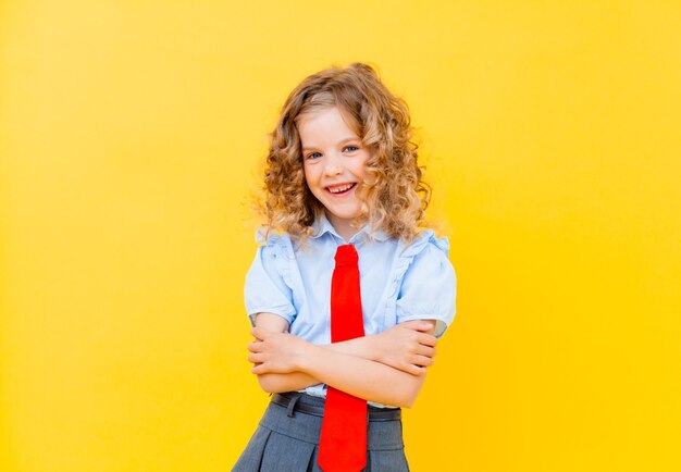 Closeup portrait girl schoolgirl on yellow background. A child from elementary school holds a textbook and points up. Education concept.