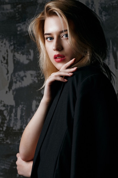 Closeup portrait of glamorous woman with perfect makeup wearing black jacket posing at studio with shadows