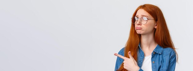 Closeup portrait gloomy and sad pouting cute redhead girl with lovely blue eyes wear glasses sulking