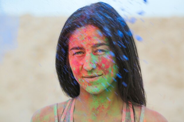 Closeup portrait of gorgeous brunette woman covered with colorful Holi paint, posing at the desert