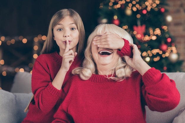 Closeup portrait of grandchild closing granny eyes surprise showing shh sign at decorated house